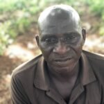 Headshot of an elderly African man wearing a grey-balck T-shirt.